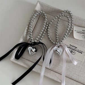 Dettaglio dell'elastico con perle d'argento con fiocco e ciondolo a cuore lucido su vassoio