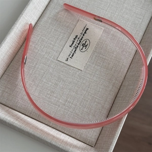 Pink translucent acetate headband with non-slip teeth shown on a beige linen display box