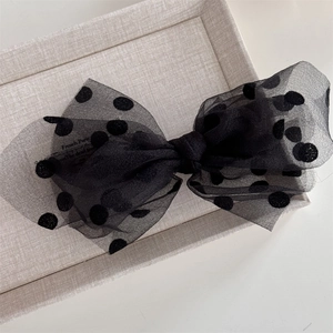 Close-up of black mesh polka dot bow hair clip with flocked texture on beige tray
