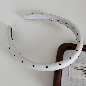 Detailed view of a white fabric headband with classic black polka dots on wooden tray
