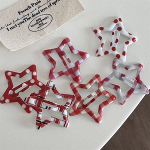 Close-up of six-piece star hair clips with red plaid and polka dot patterns on a beige base