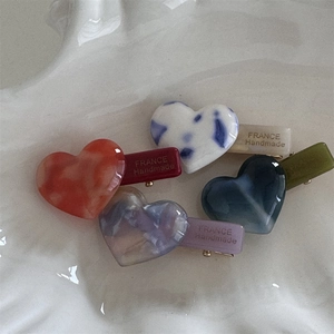 Five-piece heart acetate hair clips set in diverse colors on a decorative ceramic tray