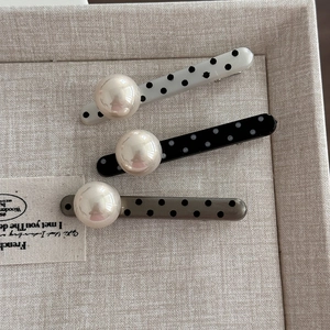 Detail of three polka dot hair clips with large pearls on a beige linen display tray