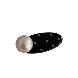 Vintage black oval hair clip with white polka dots and a large pearl accent on a white background