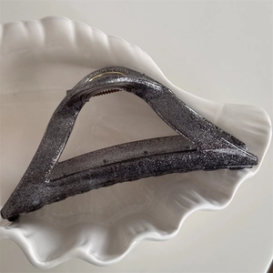 Macro detail of charcoal grey glitter triangle hair claw clip on a white shell tray