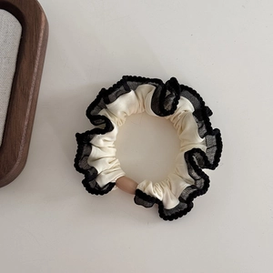 Detail of cream fabric scrunchie with black lace trim and dark brown oval bead ornament