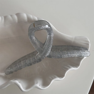 Detail of silver glitter hair claw clip with shimmering resin texture on a shell plate