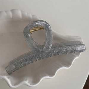 Close-up of a silver glitter hair claw clip with golden spring on a white shell plate