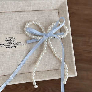 Détail de l'élégante pince à cheveux en perles avec rubans bleu clair et pompons