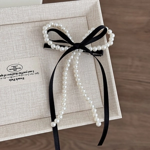 Gros plan d'une barrette nœud en ruban noir avec perles blanches et longues franges