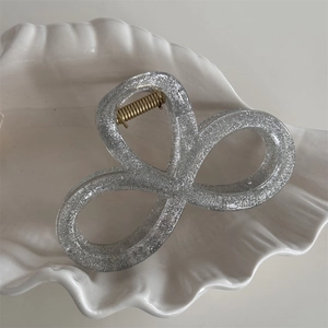 Close-up of a silver glitter hair claw clip on a white decorative shell tray