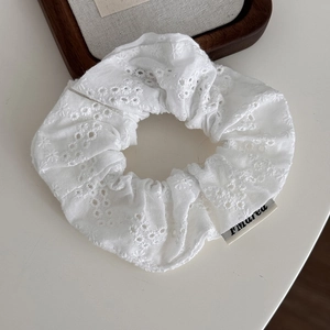 Close-up of white cotton scrunchie with intricate eyelet floral embroidery and logo tag