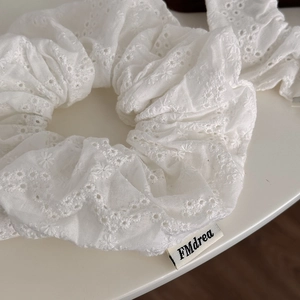 Detailed view of white floral embroidery and eyelet texture on a stylish cotton scrunchie