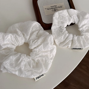 Close-up of white scrunchies with intricate floral embroidery and woven brand tags