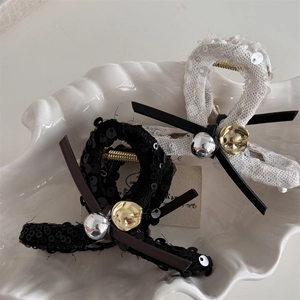 Elegant sequined bow hair claws with metallic beads in a white ceramic shell tray