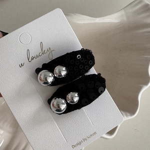 Detailed view of two black sequin bow hair clips with silver metallic beads on a display card