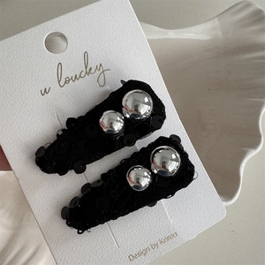 Close-up of black sequined bow hair clips with silver bead accents on display card