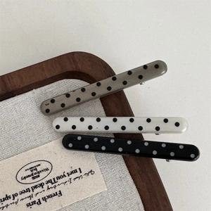 Polka dot hair clips set in grey, cream, and black colors on wooden display tray
