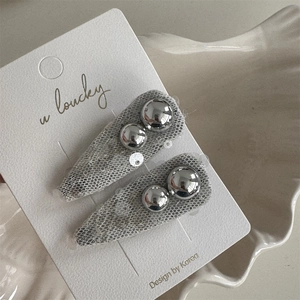 Close-up of two grey mesh hair clips with silver beads on a ceramic tray packaging