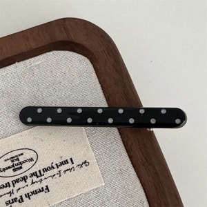 Detail of minimalist black hair clip with white polka dots on a textured fabric surface
