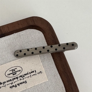 Close-up of a silver-gray polka dot metal hair clip on a vintage decorative tray