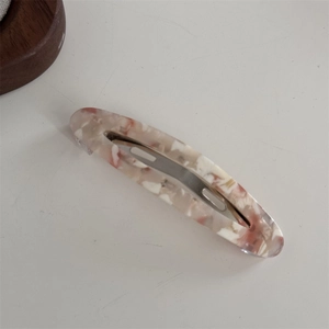 Détail d'une barrette en acétate rose et beige avec motif écaille et fermoir en métal argent