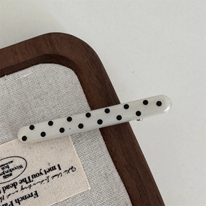 Macro detail of a white polka dot acrylic hair clip resting on a wooden jewelry tray