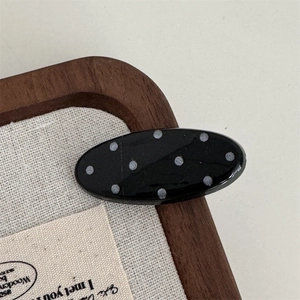 Detailed view of a black oval hair clip with white polka dots on a vintage background