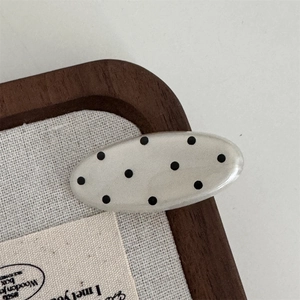 Detailed view of an oval polka dot resin hair clip on a natural canvas texture background