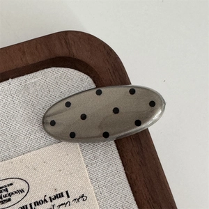 Detailed view of gray polka dot acetate hair clip on a minimalist aesthetic background