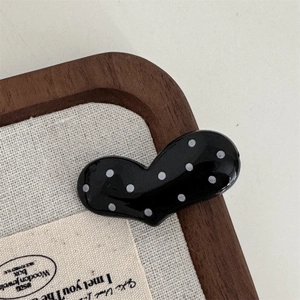 Close-up of a black heart-shaped hair clip with white polka dots on a wooden background