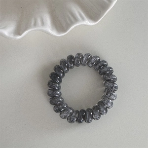 Détail de l'élastique spirale en résine effet marbre gris sur un support minimaliste épuré