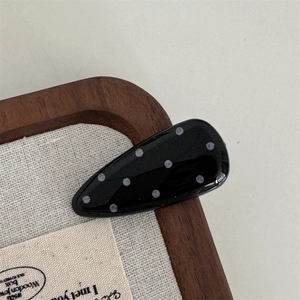 Close-up of a teardrop-shaped black hair clip with white polka dots on a wooden surface