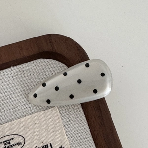Detailed view of a cream waterdrop hair clip with black polka dots on a display tray