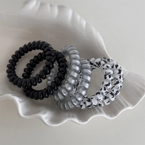Close-up of four spiral hair ties in cow print and solid colors on a shell plate