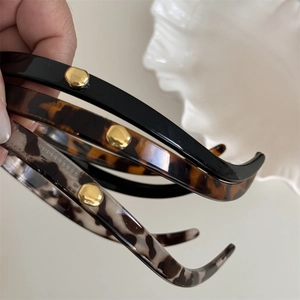 Close-up of three narrow resin headbands with leopard print and gold metal accents