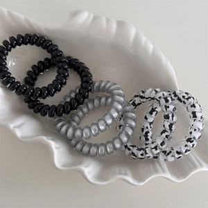 Cow pattern and solid color spiral hair ties in a shell tray with 45-degree view