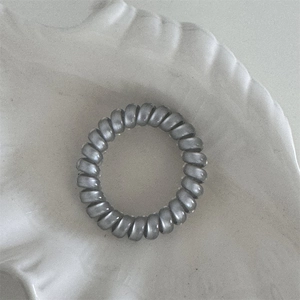 Close-up of a silver-grey spiral hair tie on a white ceramic tray with a matte finish