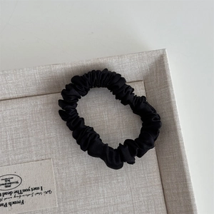 Macro detail of high-density black silk satin scrunchie with smooth pleated texture