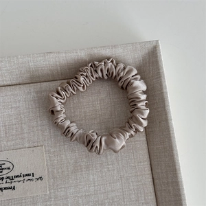 Close-up of champagne silk scrunchie on linen tray showing smooth satin texture