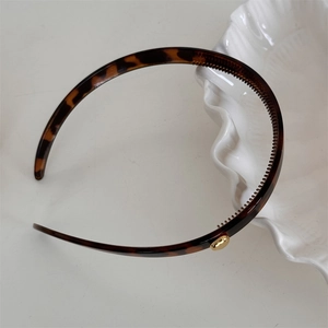 Detail of slim tortoiseshell headband featuring anti-slip teeth and a gold metal accent