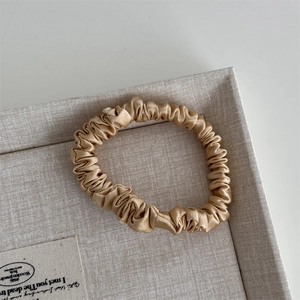 Detail of champagne gold silk scrunchie with soft satin texture in a linen tray