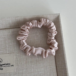Detail of soft pink silk satin scrunchie with pleated texture on beige fabric tray