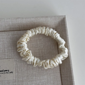 Detailed texture of ivory silk scrunchie with soft sheen on a textured display tray