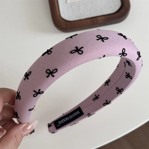 Gros plan détaillé du serre-tête rose en éponge avec motifs nœuds et étiquette faite main