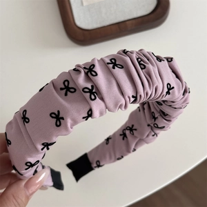 Gros plan d'un serre-tête rose froncé avec motifs nœuds noirs et texture de tissu doux