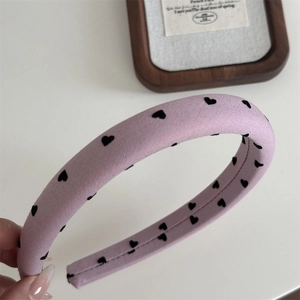 Détail d'un serre-tête en éponge violet clair avec motifs de cœurs noirs et tissu doux
