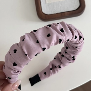 Détail d'un serre-tête éponge rose clair avec motif de cœur noir et tissu plissé