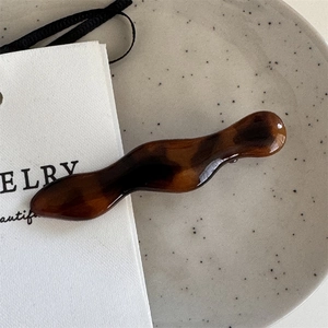 Macro detail of wavy tortoise shell hair clip with deep brown resin texture on ceramic tray