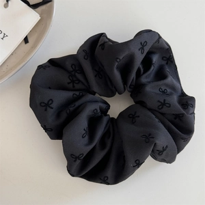Detailed macro view of black scrunchie with embroidered bow patterns and silky texture